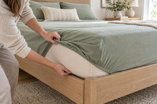 Person pulling a sage fitted sheet securely beneath a mattress corner